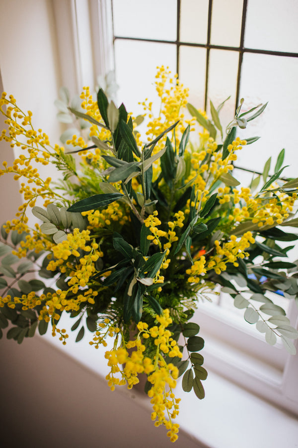 An abundance of artificial mimosa, olive branches and soft grey foliage arranged in a chic off white vase or available as a gift wrapped bouquet.  Perfect for the home or to gift.
