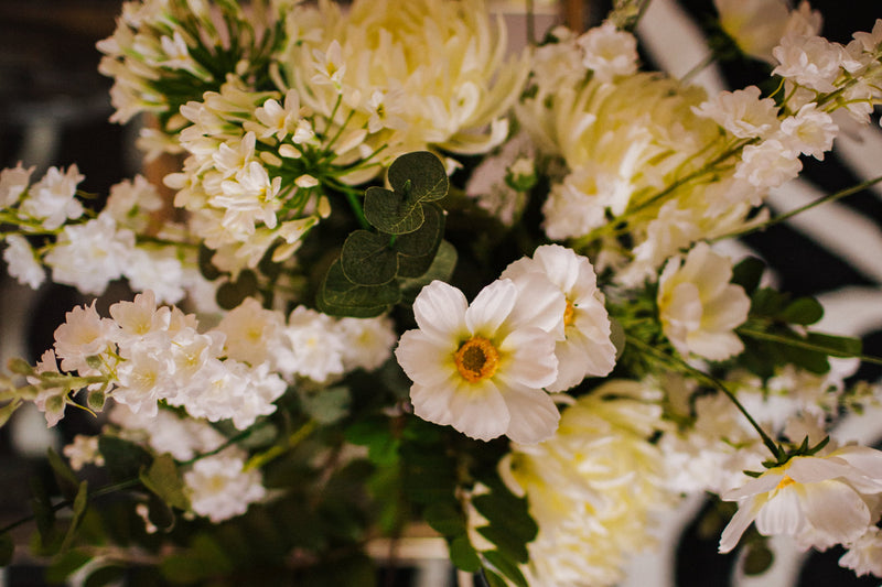 Luxury artificial white cosmos, delphinium, agapanthus and chrysanthemums mingled with the highest quality robinia and eucalyptus. Expertly arranged by our team of florists into a choice of white ceramic or green glass vase or available as a beautifully wrapped bouquet.