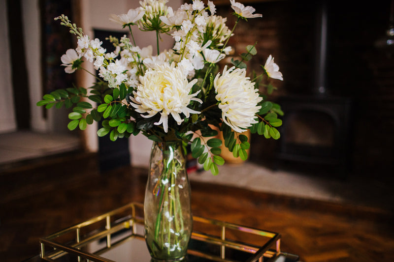 Luxury artificial white cosmos, delphinium, agapanthus and chrysanthemums mingled with the highest quality robinia and eucalyptus. Expertly arranged by our team of florists into a choice of white ceramic or green glass vase or available as a beautifully wrapped bouquet.