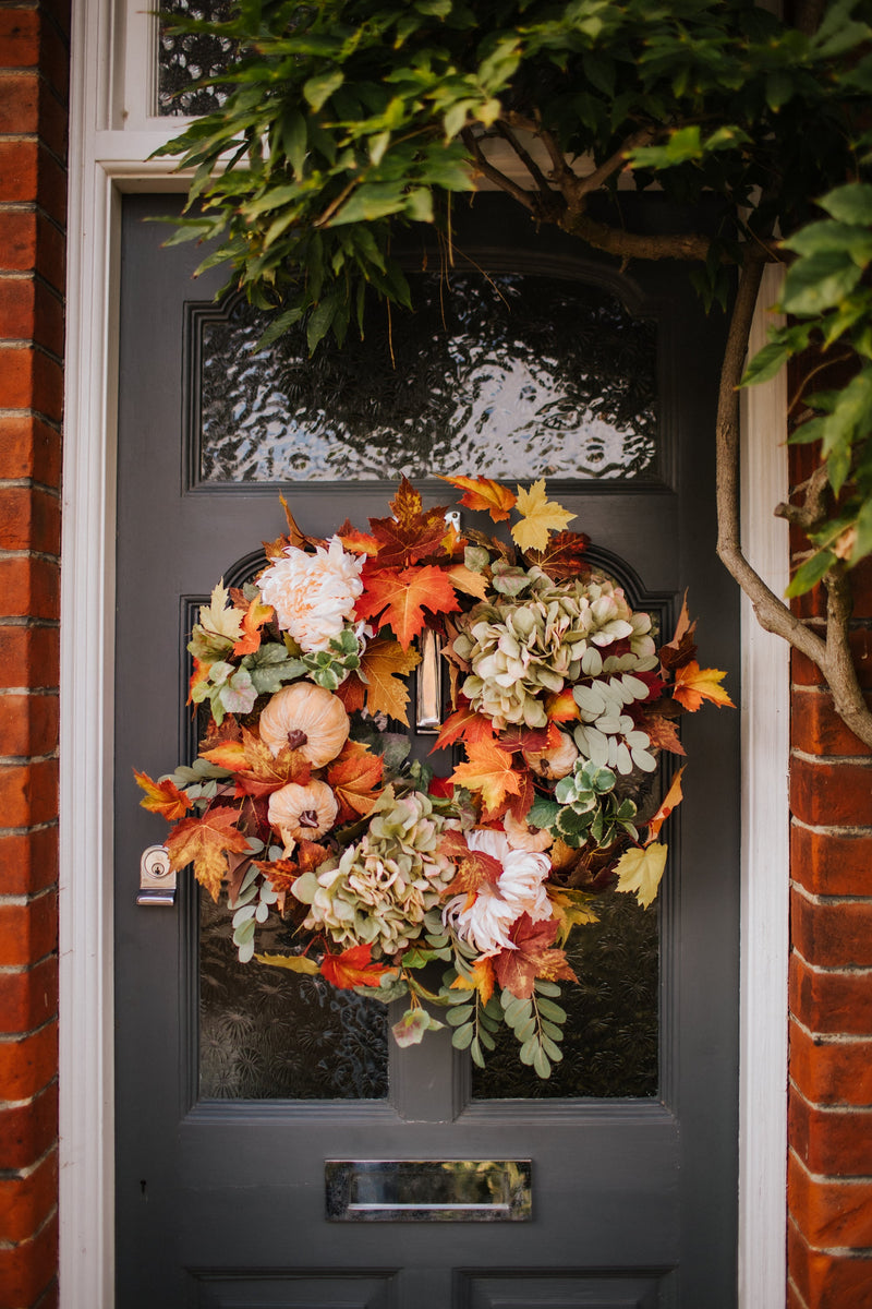 An eye catching abundance of autumnal foliage paired with silky cream and blush pink hydrangea, blooms and pumpkins in a celebration of the amazing colours and textures of the season.    This luxurious faux wreath has been created by our team of skilled florists ready to add instant warmth and comfort to any space.