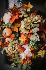 An eye catching abundance of autumnal foliage paired with silky cream and blush pink hydrangea, blooms and pumpkins in a celebration of the amazing colours and textures of the season.    This luxurious faux wreath has been created by our team of skilled florists ready to add instant warmth and comfort to any space.