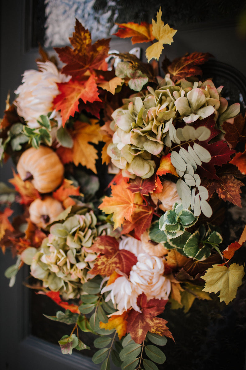 An eye catching abundance of autumnal foliage paired with silky cream and blush pink hydrangea, blooms and pumpkins in a celebration of the amazing colours and textures of the season.    This luxurious faux wreath has been created by our team of skilled florists ready to add instant warmth and comfort to any space.