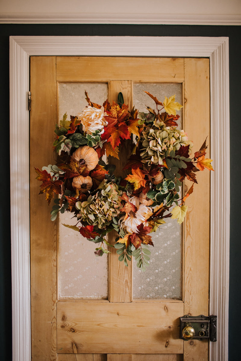 An eye catching abundance of autumnal foliage paired with silky cream and blush pink hydrangea, blooms and pumpkins in a celebration of the amazing colours and textures of the season.    This luxurious faux wreath has been created by our team of skilled florists ready to add instant warmth and comfort to any space.