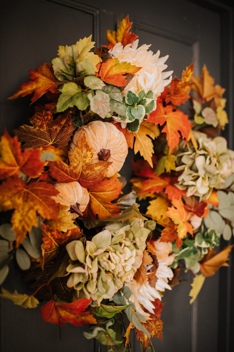 An eye catching abundance of autumnal foliage paired with silky cream and blush pink hydrangea, blooms and pumpkins in a celebration of the amazing colours and textures of the season.    This luxurious faux wreath has been created by our team of skilled florists ready to add instant warmth and comfort to any space.